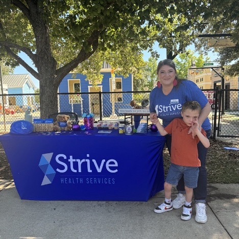 Strive employee and child at an outdoor event table